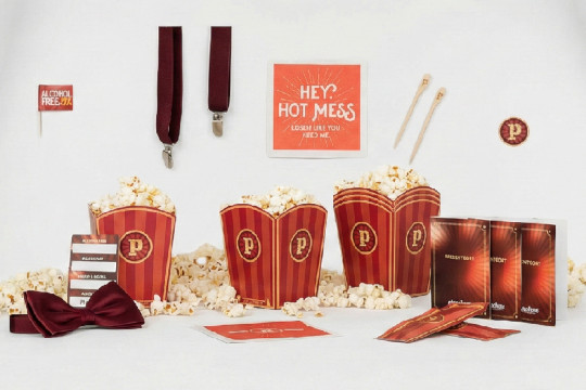 Ett urval av profilprodukter från Pinchos med deras karaktäristiska cirkustema. Bilden visar röd- och guldrandiga popcornbägare fyllda med popcorn, presentkort, en röd fluga, hängslen, våtservetter samt en skylt med texten "Hey hot mess".
