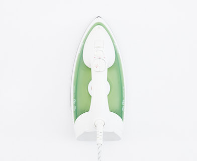 Ett strykjärn med grön handtag på en vit yta.