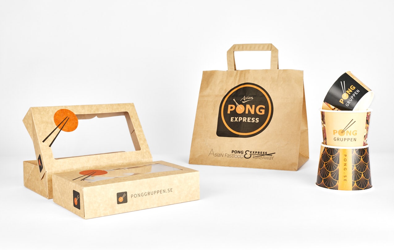 Take away-förpackningar från Pong Express i brunt kraftpapper med svarta detaljer. Bilden visar rektangulära matlådor med tittfönster och ätpinnar som grafiskt element, en papperskasse med logotypen "Asian Pong Express", samt staplade bägare med ett solfjädersmönster i svart och guld.