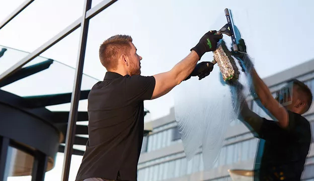 Man rengör fönster med fönsterskrapa