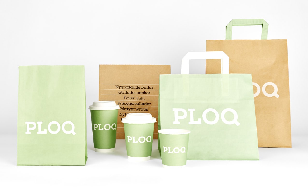 En kollektion av Ploqs förpackningar i en ljusgrön och brun färgskala. Motivet visar papperskassar med vita handtag och texten "PLOQ", matchande gröna kaffemuggar, samt en brun påse med en meny som listar "Nygräddade bullar", "Grillade mackor" och "Färsk frukt".